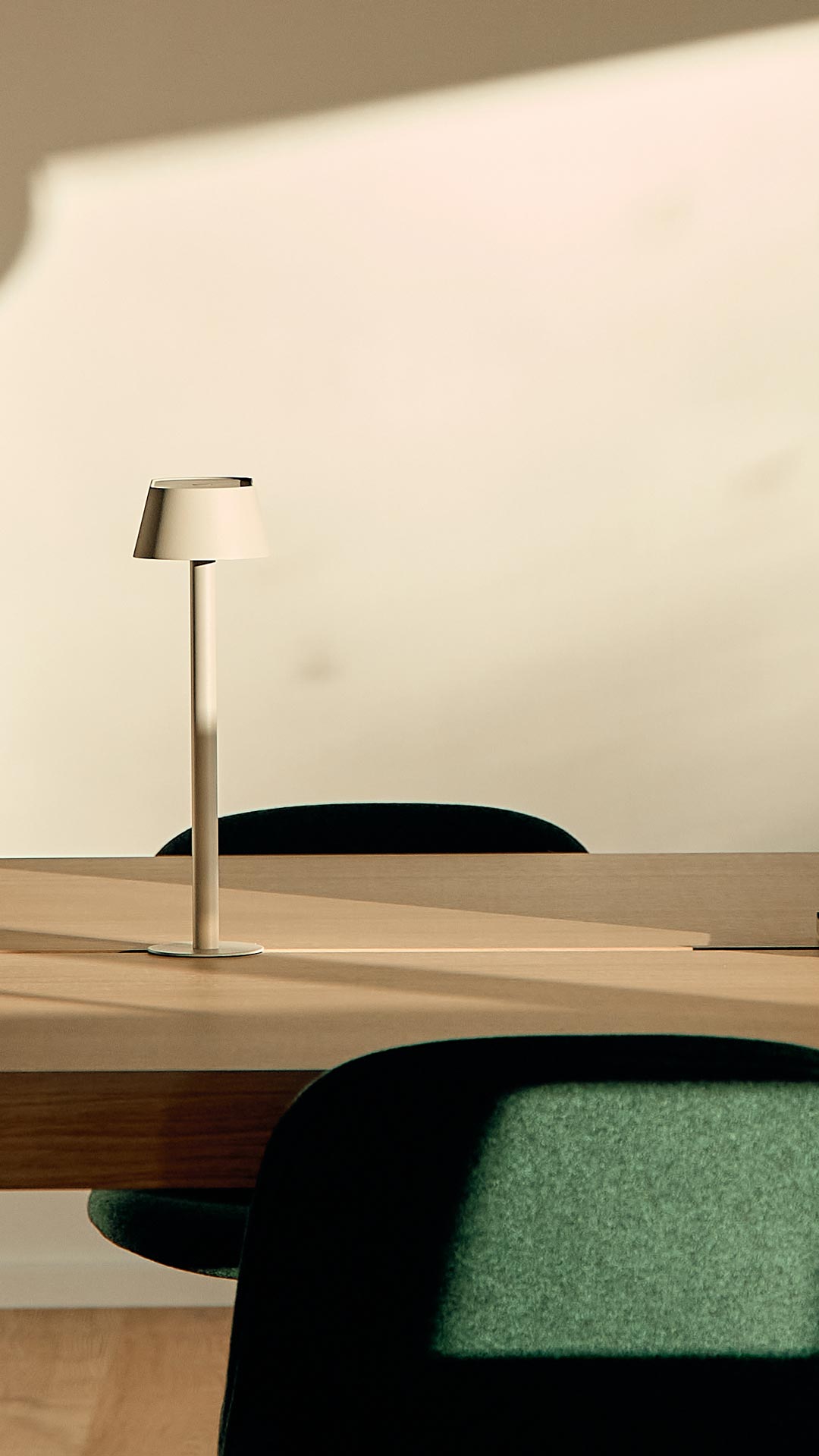 Moderne kontorplads med skrivebord i lyst eg og grønne designerstole samt enkel og stilfuld lampe.
