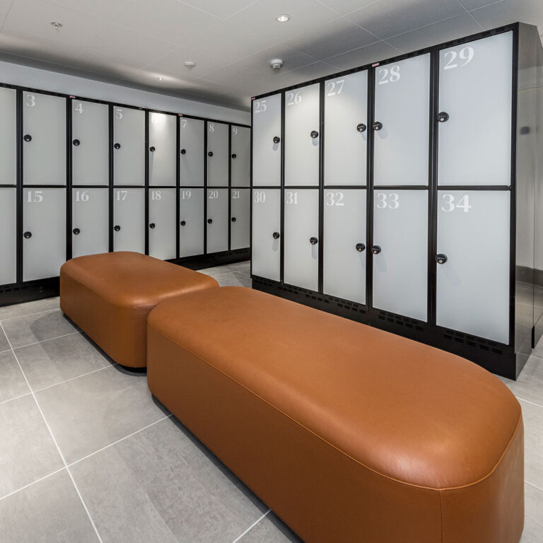 Omklædningsfaciliteter med lockers og moderne bænk i brun læder.